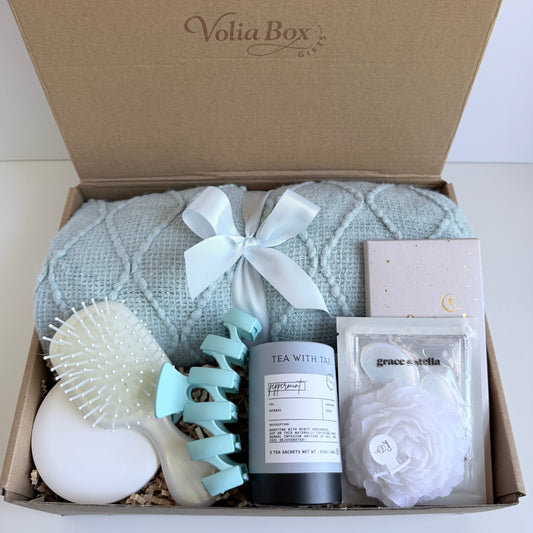 Self care gift set flat lay with eye patches, hair clip, mirror, candle, tea and chocolate