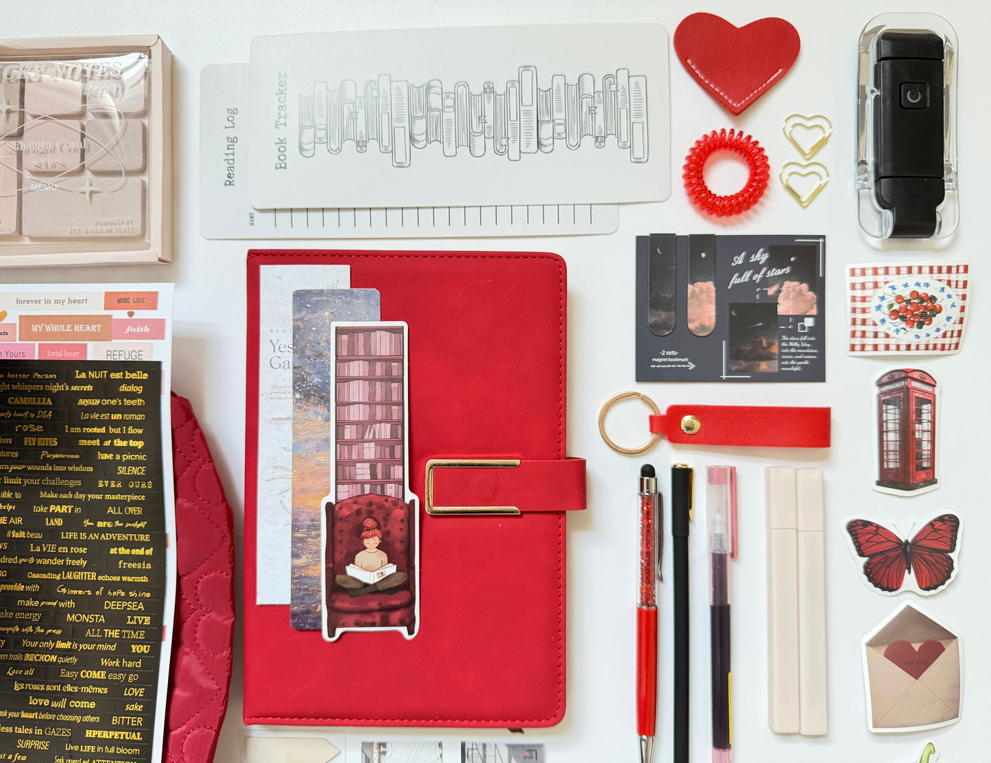 Collection of stationery items including a red planner, pens, and decorative elements on a white background.